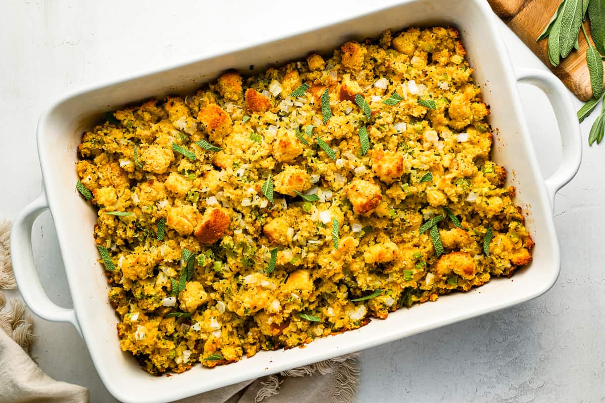 A white dish with cornbread stuffing and herbs on it.