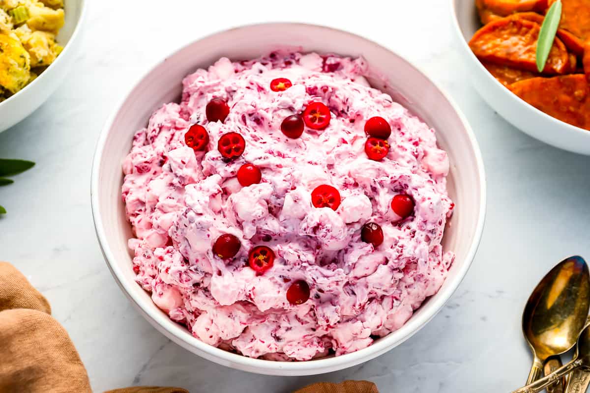 cranberry fluff salad in a white bowl with cranberries on top.