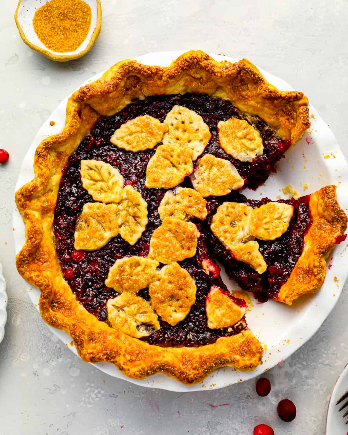A cranberry pie topped with leaf- and acorn-shaped pie crust pieces; one slice is taken out.