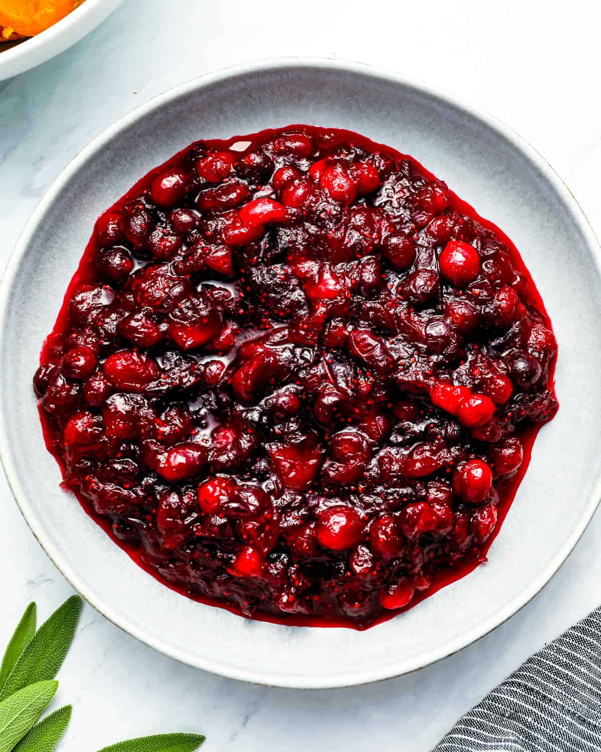Cranberry sauce in a bowl with sprigs of sage.