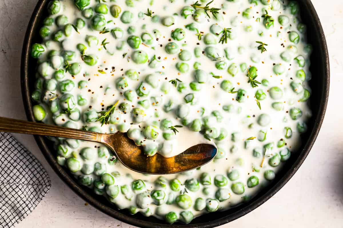 Creamed peas in white sauce in a black bowl with a spoon.