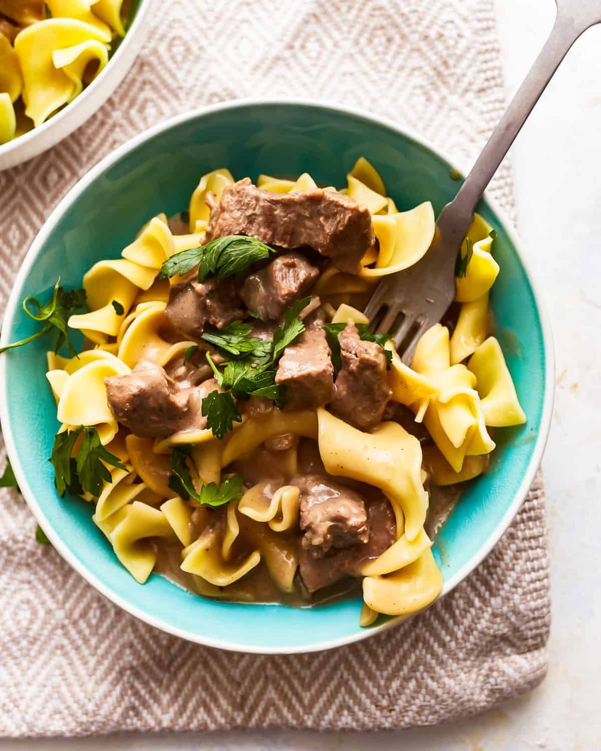 Beef and noodles in a blue bowl with a fork.