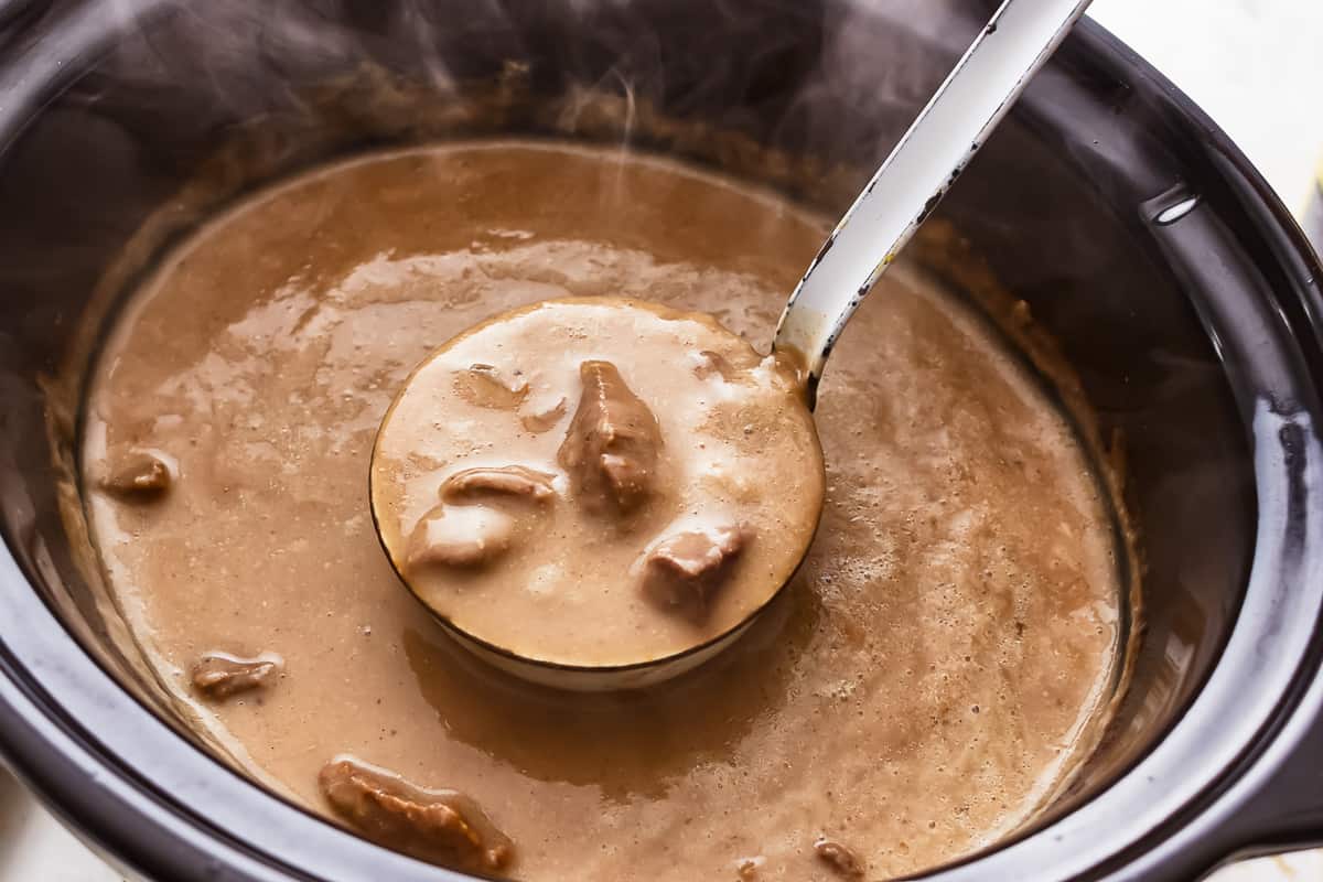 A crock pot full of gravy with a spoon in it.