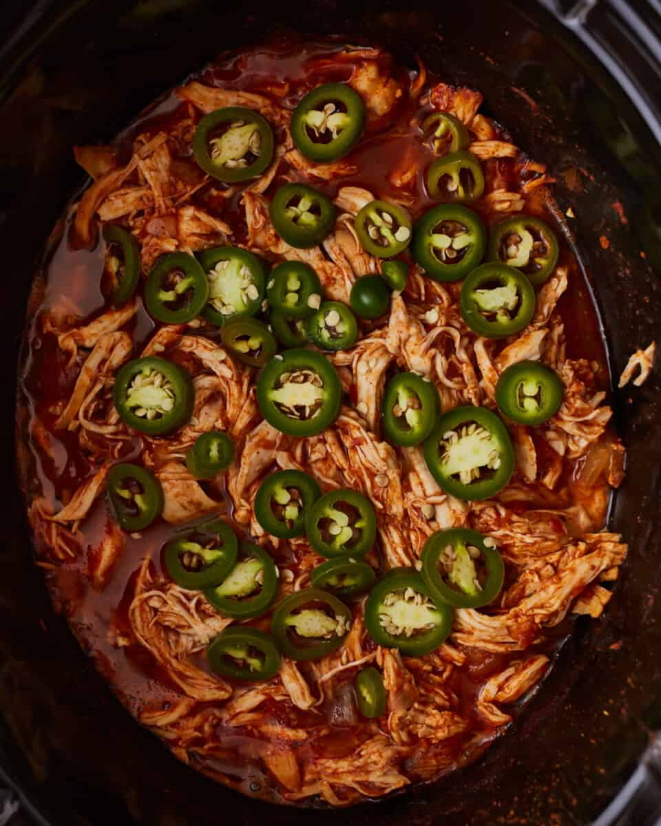 A crock pot filled with chicken and jalapenos.