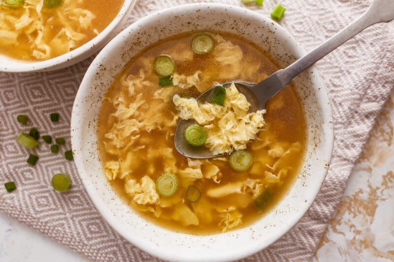Two bowls of soup with noodles and green onions and a spoon.