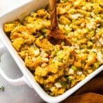Thanksgiving stuffing in a white dish with a wooden spoon.
