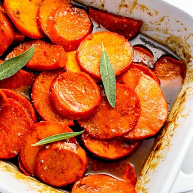 Roasted sweet potatoes in a baking dish with sage sprigs.
