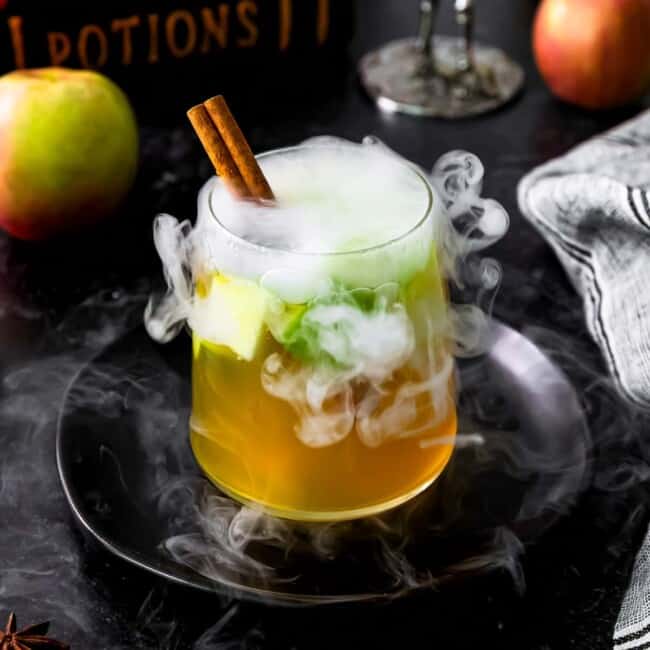 A drink with cinnamon sticks and apples on a black background.