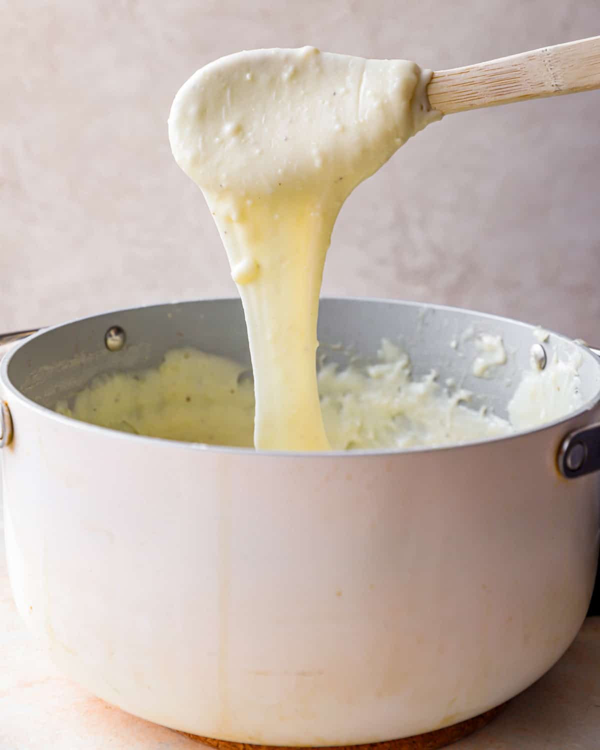 Wooden spoon pulling cheesy fondue mashed potatoes out of a pot.