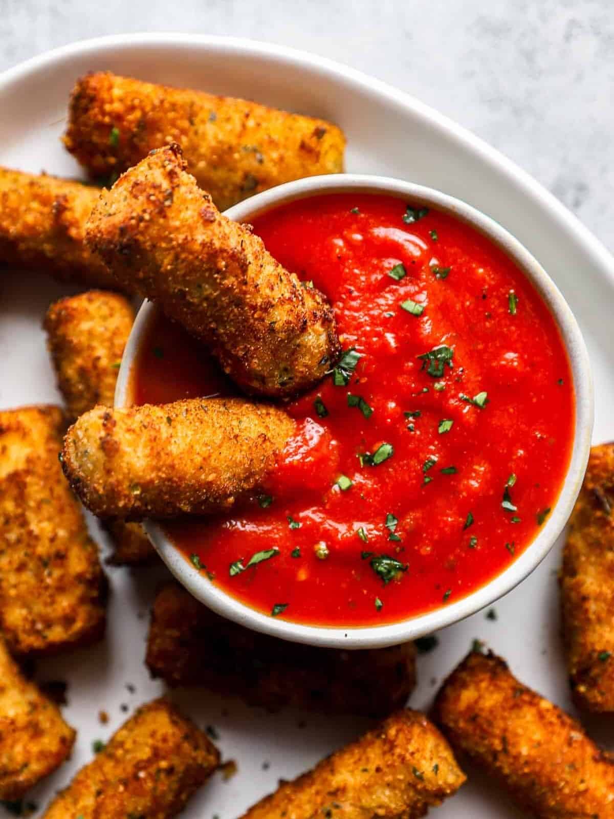 overhead view of 2 mozzarella cheese sticks dipped in a bowl of marinara sauce.