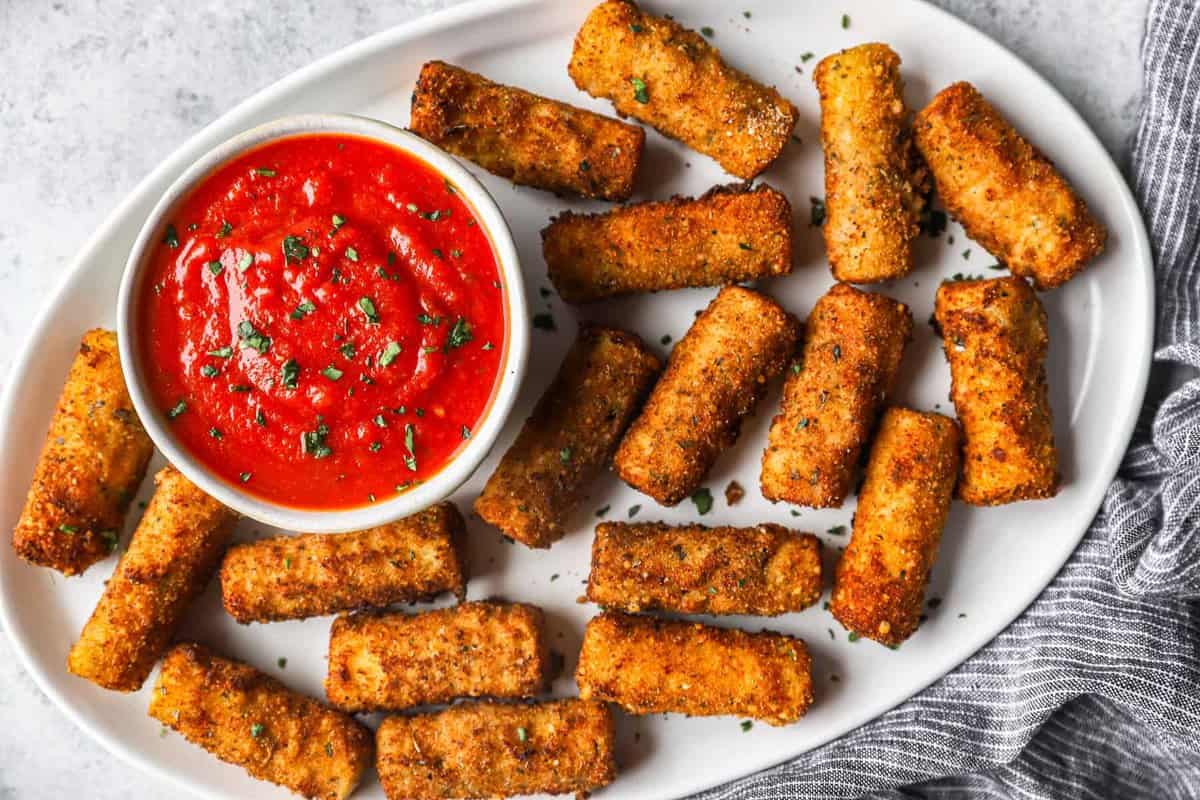 overhead view of fried mozzarella sticks on a white serving platter with a small bowl of marinara sauce.