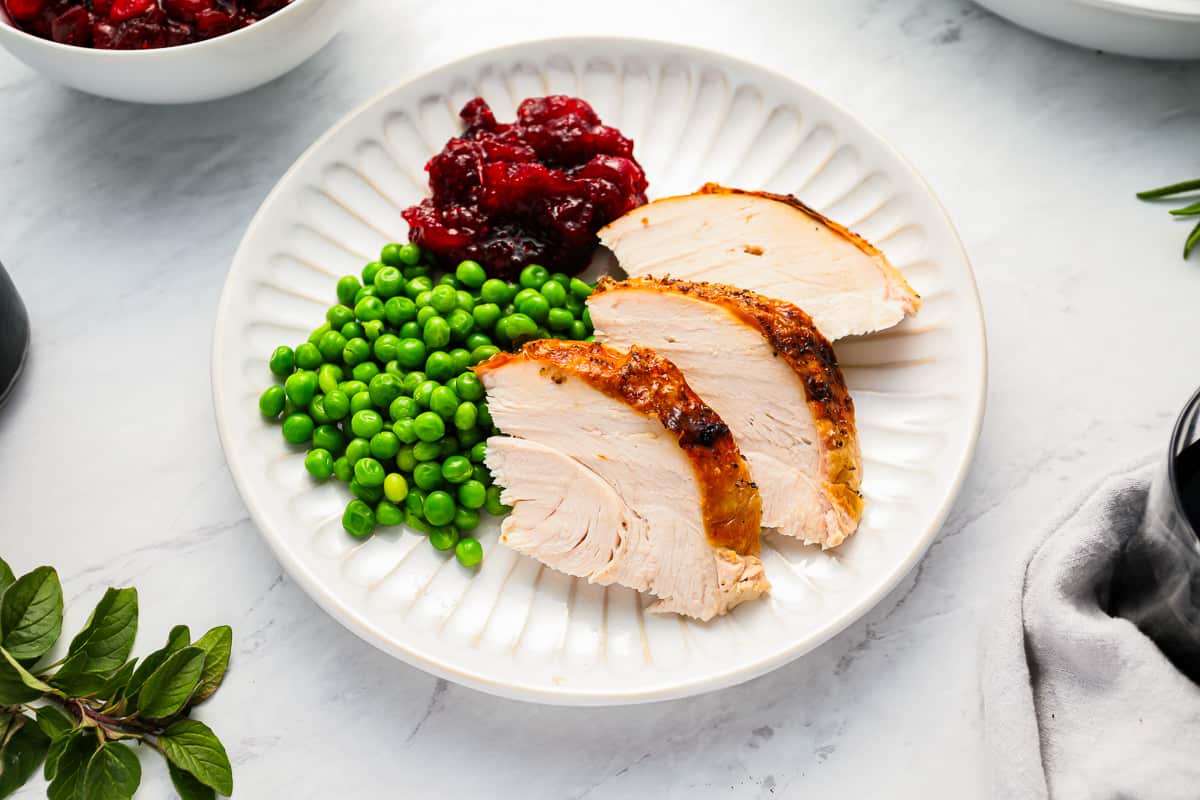 Slices of turkey with peas and cranberry sauce on a white plate.