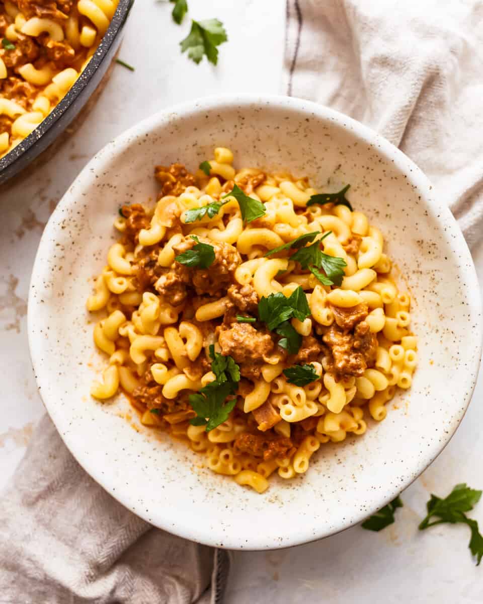 A bowl of macaroni and cheese with meat and parsley.