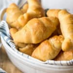 Homemade crescent rolls in a white bowl on a wooden table.