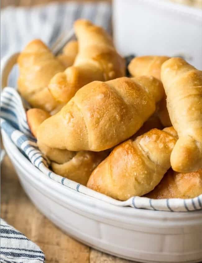 Homemade crescent rolls in a white bowl on a wooden table.