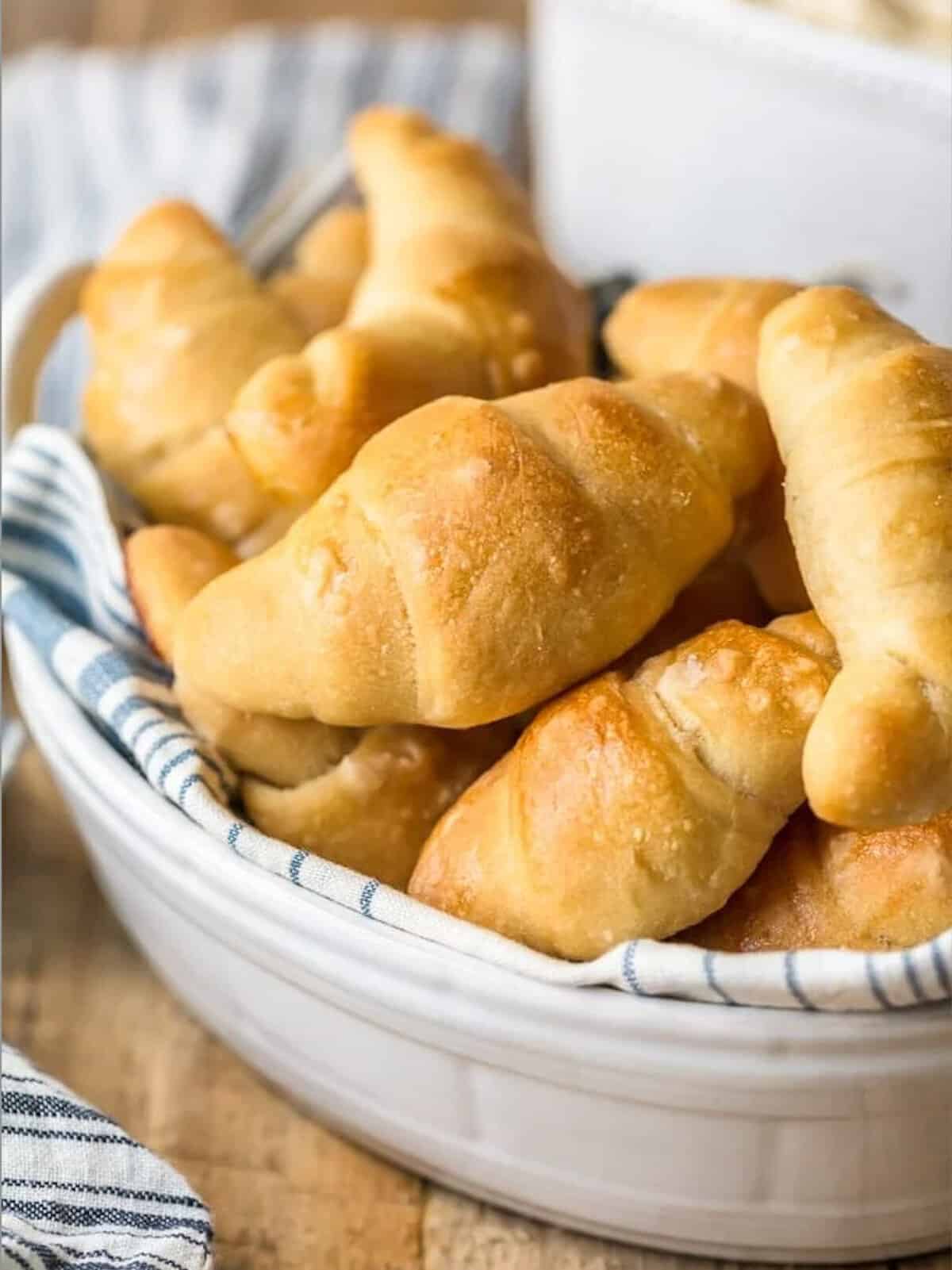 Homemade crescent rolls in a white bowl on a wooden table.