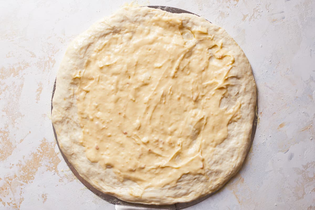 raw pizza dough with alfredo sauce spread on top.
