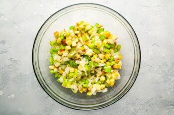 A glass bowl filled with corn and green onions.