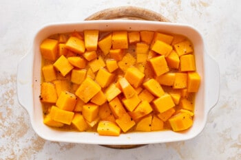 Squash cubes in a white baking dish on a white background.