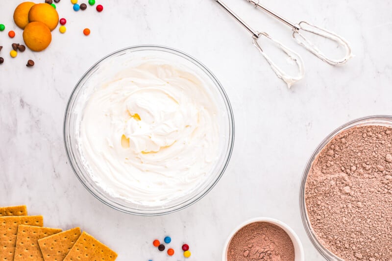 A bowl of whipped cream, a bowl of chocolate chips, and a bowl of graham crackers.