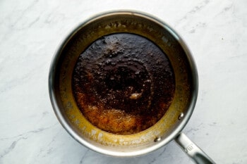 A frying pan with brown oil on a marble countertop.