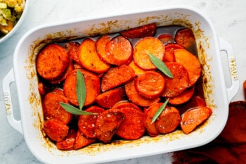 Roasted sweet potatoes in a white dish with sage.