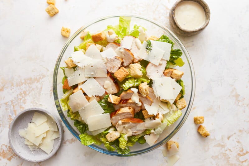 A bowl of chicken caesar salad with croutons and parmesan cheese.