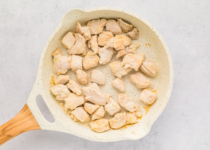 Chicken in a pan with a wooden spoon.