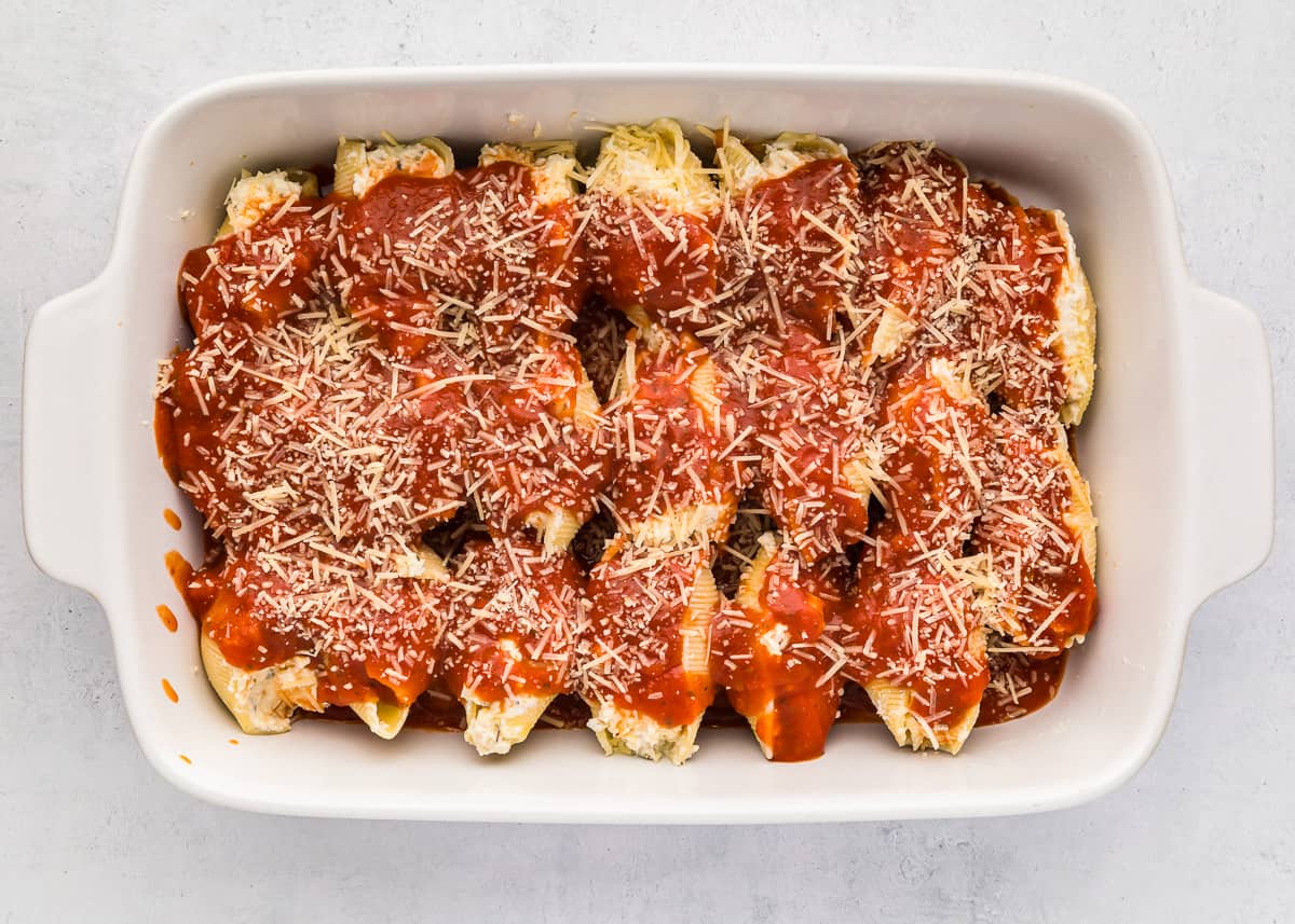 Chicken stuffed shells with sauce and cheese in a white baking dish.