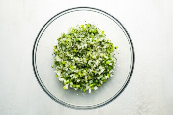 A glass bowl filled with chopped greens on a white surface.