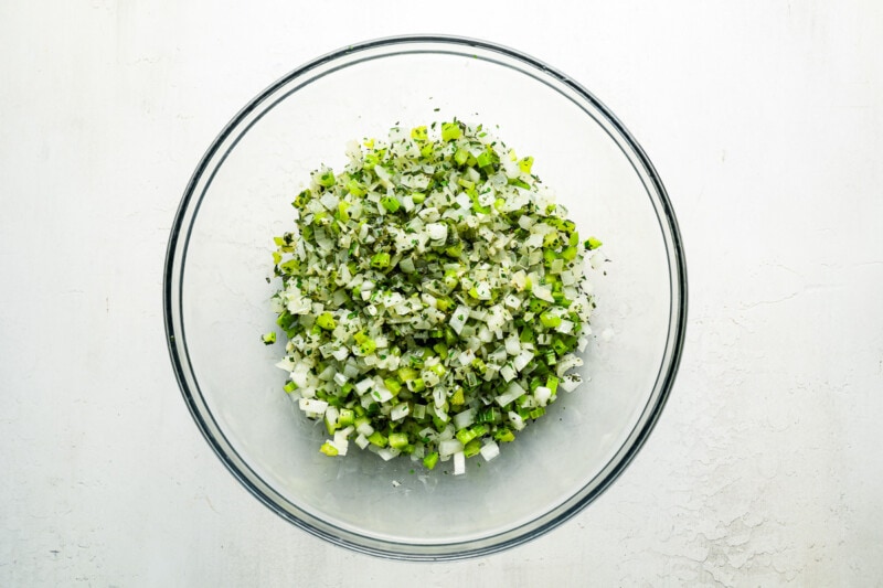 A glass bowl filled with chopped greens on a white surface.