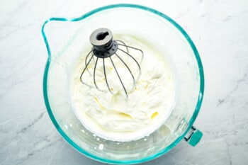 Whipped cream in a glass bowl with a whisk.