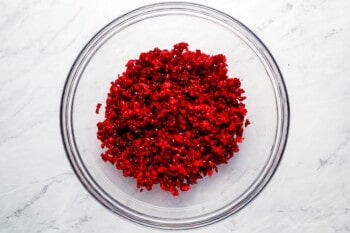 Cranberries in a glass bowl on a marble countertop.