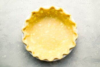 A pie crust in a white bowl on a gray surface.