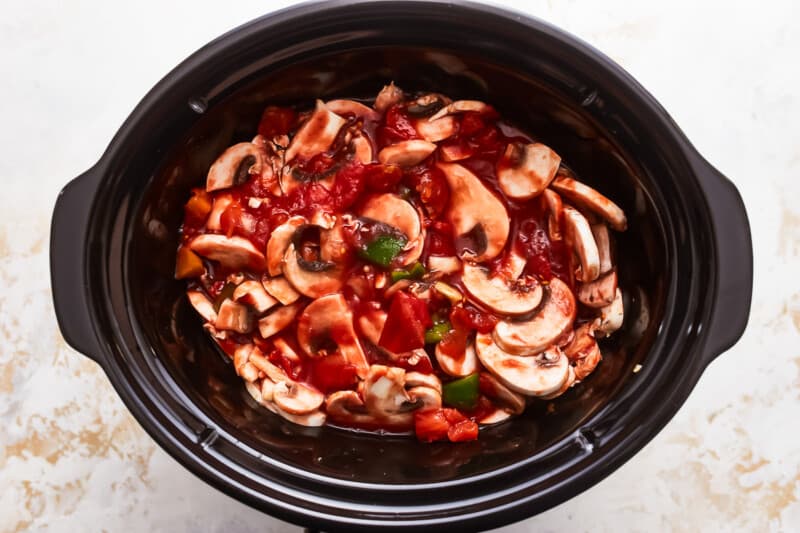 A crock pot filled with mushrooms and sauce.