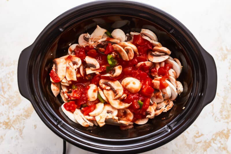 A crock pot filled with tomatoes and mushrooms.