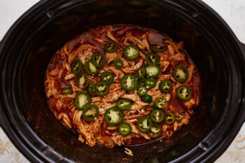 A slow cooker filled with chicken and jalapenos.