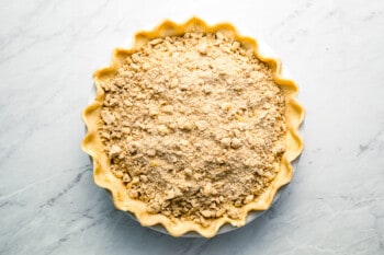 A pie crust with crumble topping on a marble surface.
