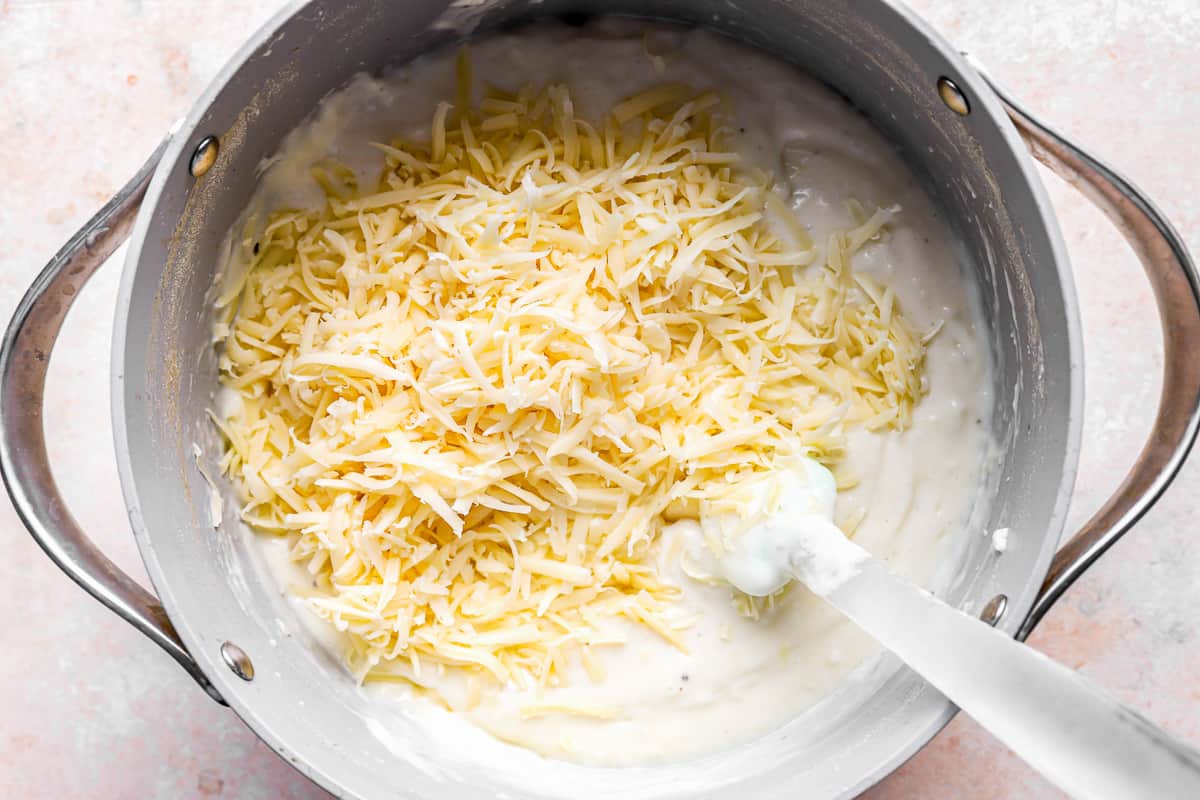grated cheese in a pot of mashed potatoes with a rubber spatula.