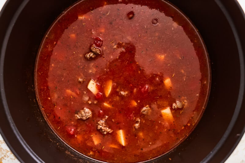 A crock pot full of soup with meat in it.