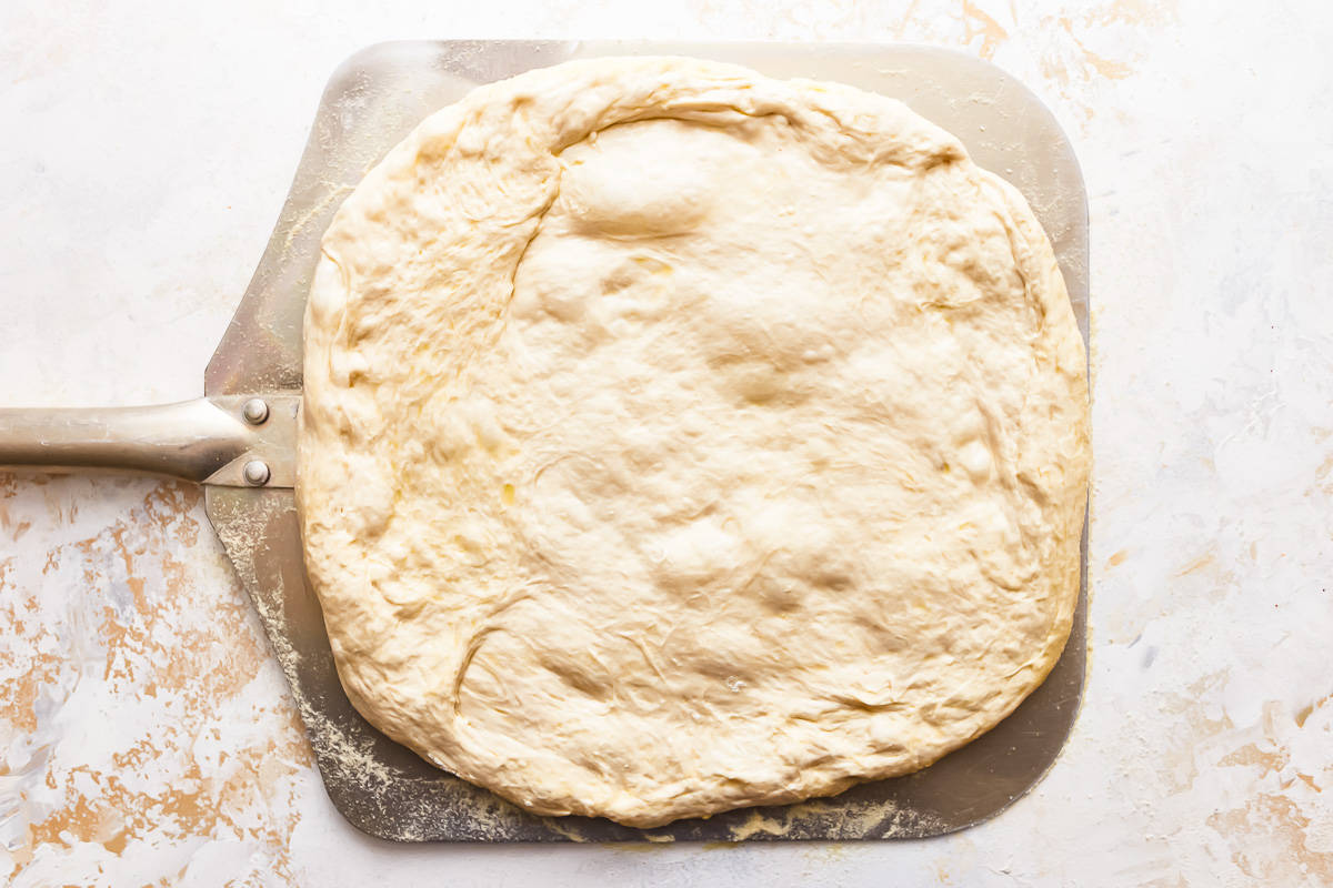 A pizza dough on a metal pan with a spatula.