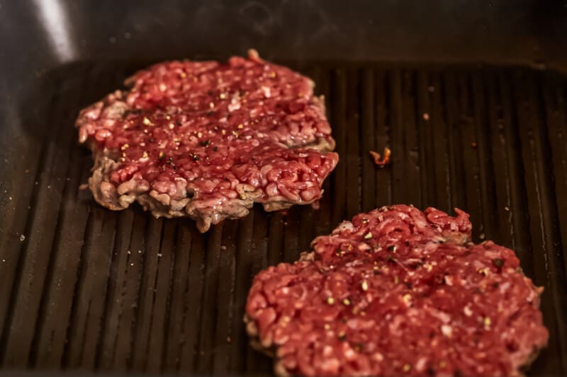 Two beef burgers being cooked on a grill.