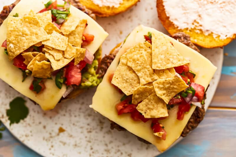 Two burgers with toppings on a plate.