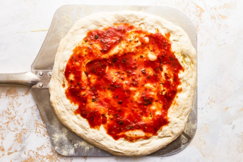 A pizza with sauce on a baking sheet.