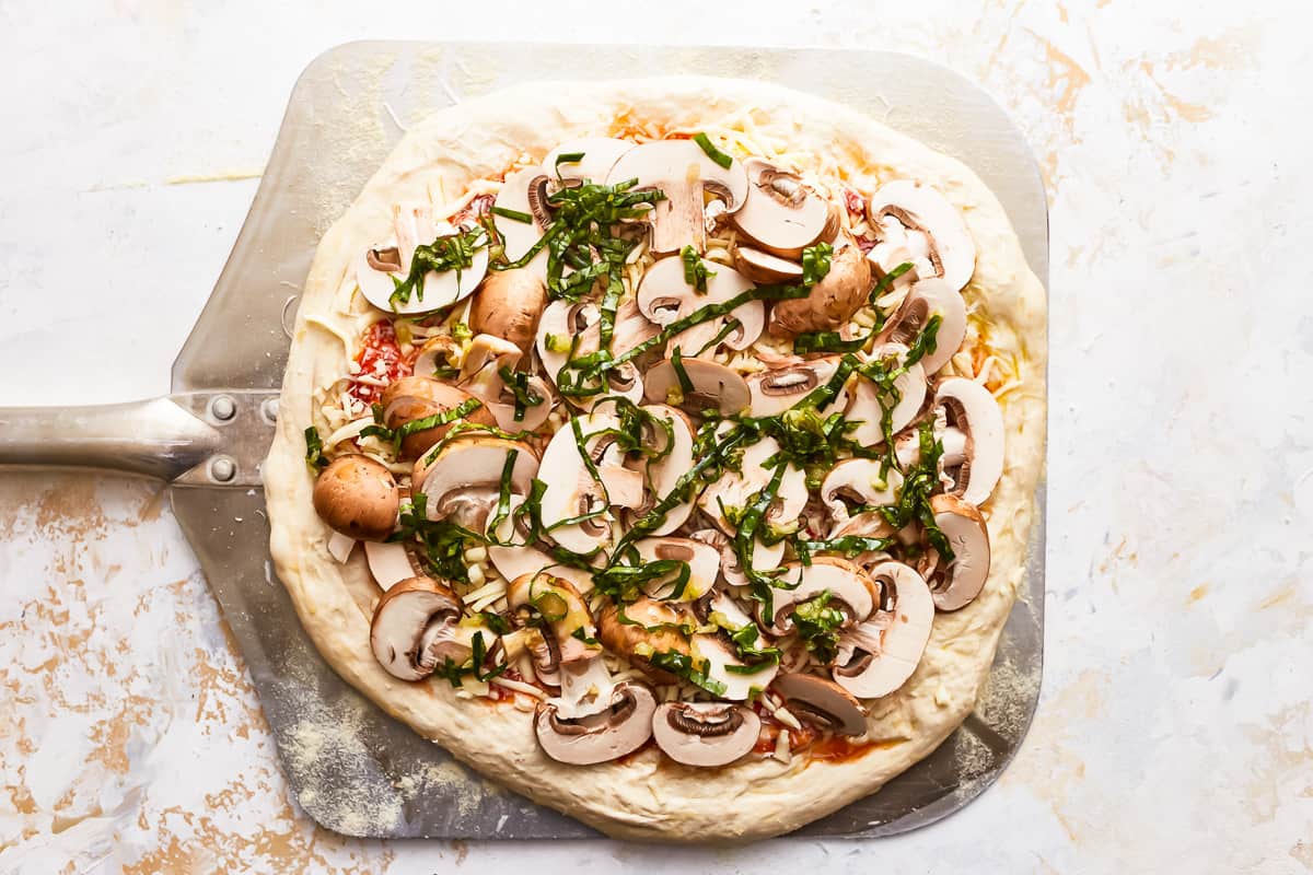 A pizza with mushrooms and basil on it.
