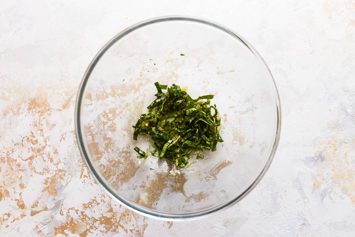 A glass bowl filled with basil, garlic, and olive oil.