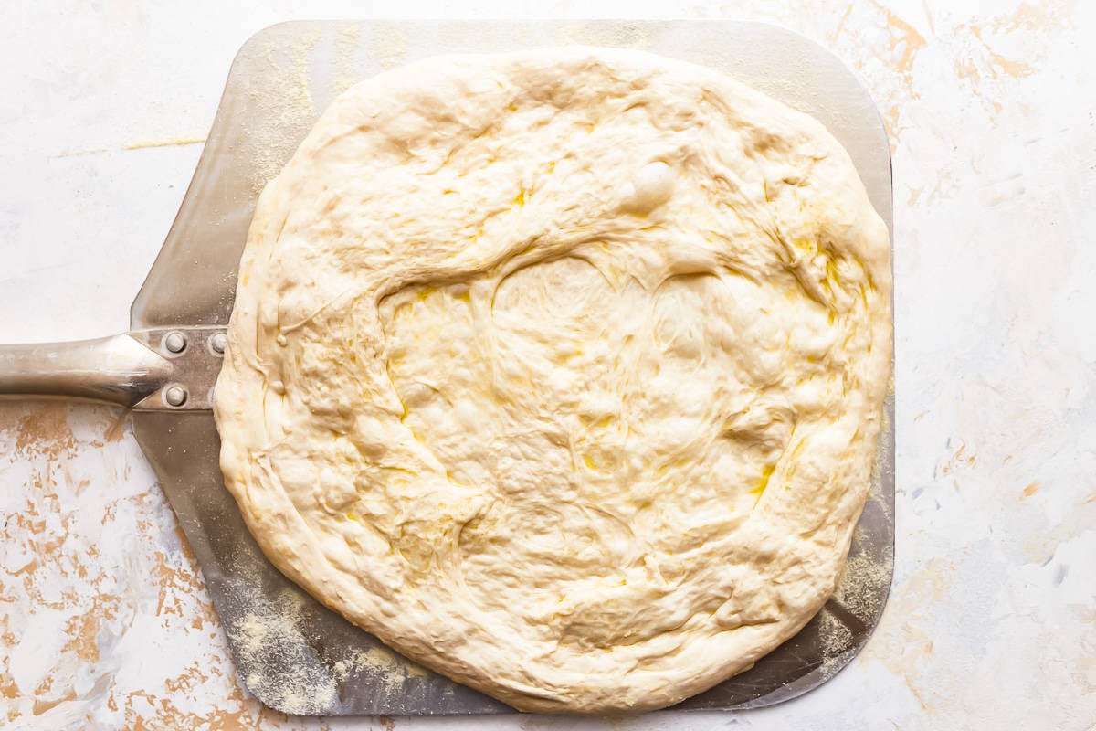 A pizza dough on a metal pan with a spatula.