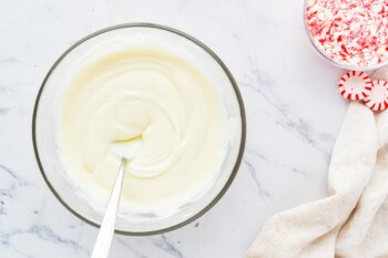 A bowl of whipped cream with a spoon and peppermint candies.