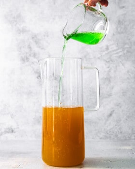 A person pouring orange juice into a pitcher.