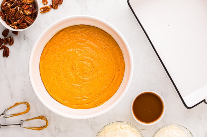 A bowl of mashed sweet potatoes with pecans and butter on a marble countertop.